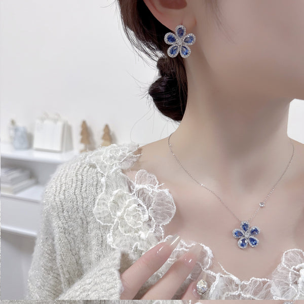 Elegant jewelry set with a silver-tone necklace and matching stud earrings, featuring blue and clear floral gemstones.