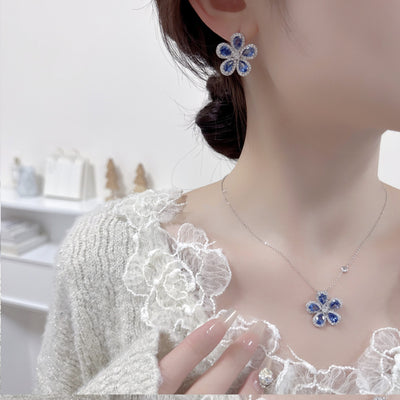 Elegant jewelry set with a silver-tone necklace and matching stud earrings, featuring blue and clear floral gemstones.