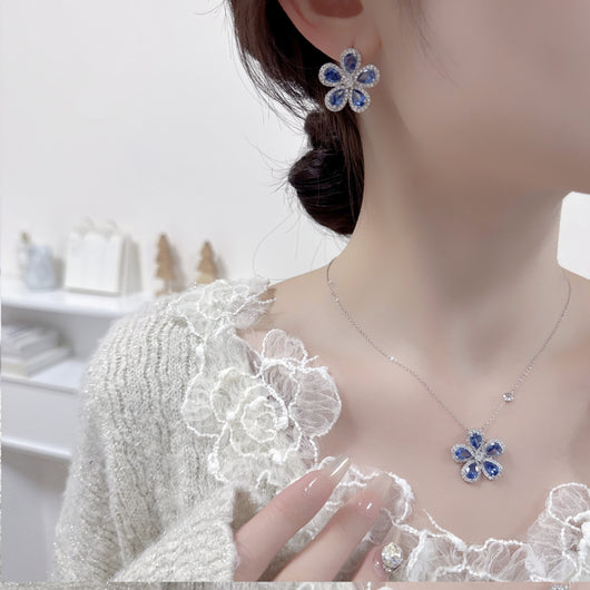 Elegant jewelry set with a silver-tone necklace and matching stud earrings, featuring blue and clear floral gemstones.