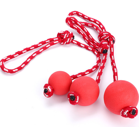 Three red rubber pet balls of varying sizes, attached to a red and white braided rope, for chewing and play.