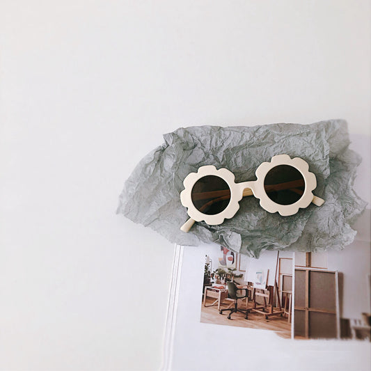 Cream flower-shaped sunglasses for babies and toddlers with dark lenses, displayed on crumpled grey paper. - Image 2