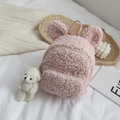 Pink fuzzy mini backpack with bear ears and a small white teddy bear keychain on a white bed. - Image 17