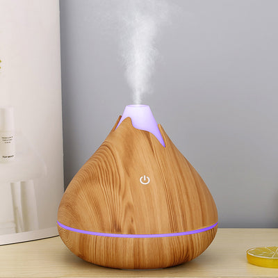Teardrop-shaped aromatherapy humidifier with light wood grain finish, emitting mist and glowing with purple LED light. - Image 13