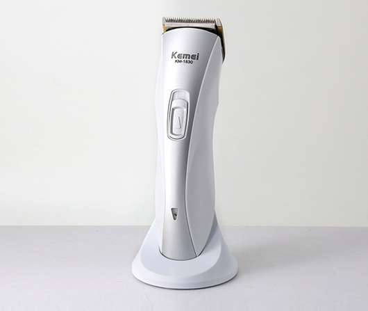White and silver Kemei KM-1830 electric hair clipper with a charging base on a light background.