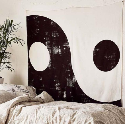 Black and white Yin Yang tapestry with a distressed finish, hung above a bed in a modern bedroom.
