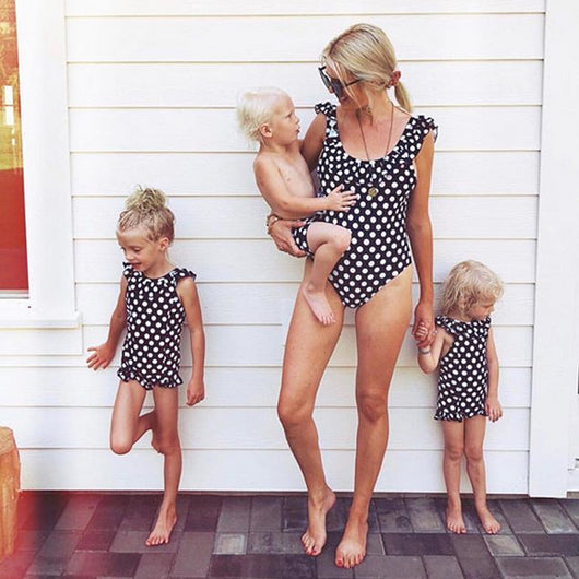 Mother and three children in matching black and white polka dot one-piece swimsuits with ruffled straps.