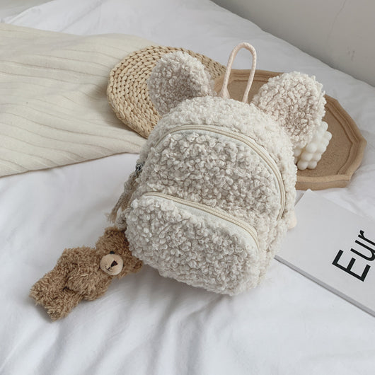 Pink fuzzy mini backpack with bear ears and a small white teddy bear keychain on a white bed. - Image 16