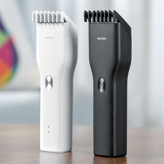 Black cordless hair shaver with a comb attachment and two white indicator lights, with a blurred white shaver in the background.