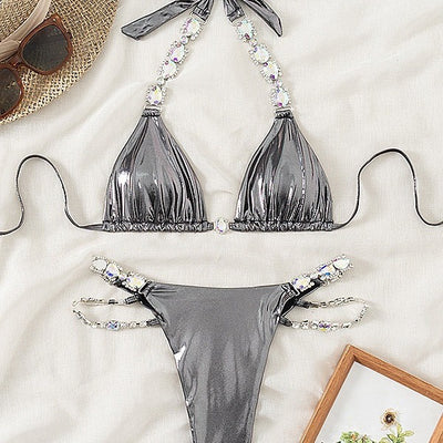 Shiny blue two-piece bikini with rhinestone-embellished halter top and high-cut bottom, laid flat with a straw hat and sunglasses. - Image 4