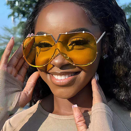 Oversized V-shaped sunglasses with a gold metal frame, white accents, clear lenses, and decorative rivets.