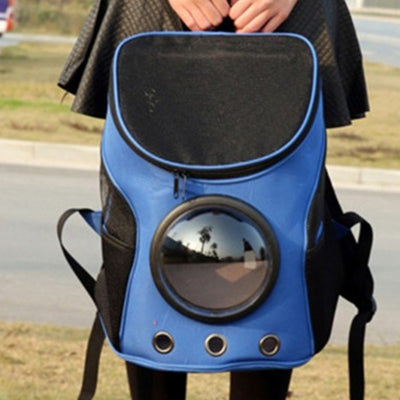 Blue and black pet carrier backpack with a clear bubble window, mesh sides, and ventilation holes, carried by a person outdoors. - Image 3