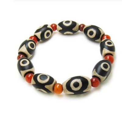 Three-eyed Dzi bead bracelet with alternating black and cream oval Dzi beads and round red agate beads.