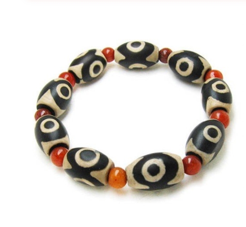 Three-eyed Dzi bead bracelet with alternating black and cream oval Dzi beads and round red agate beads.