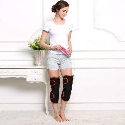 Woman sitting on a rug, using black and orange electric heating knee and leg massagers with a remote control. - Image 2
