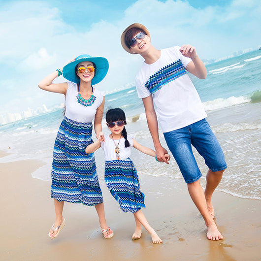 Family of four wearing matching white and blue striped outfits on a sunny beach, smiling at the camera.