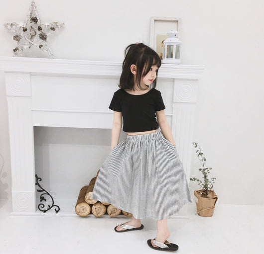 Young girl wearing a black short-sleeve crop top and a grey and white striped midi skirt with flip-flops. - Image 5