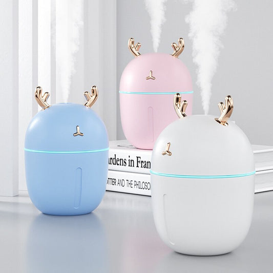 Pink deer-shaped mini humidifier with gold antlers and a glowing blue light band, on a pink background.