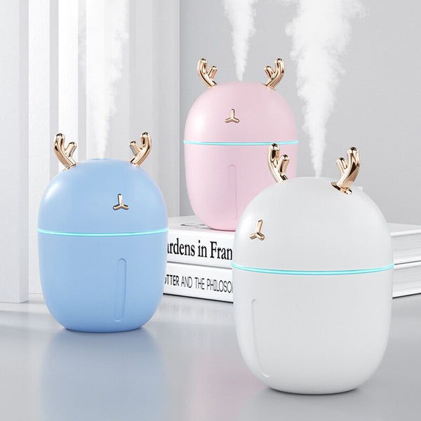 Pink deer-shaped mini humidifier with gold antlers and a glowing blue light band, on a pink background.