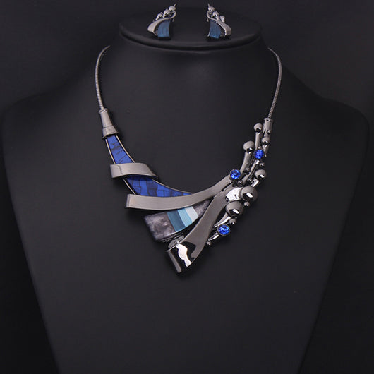 Luxury geometric necklace and earring set with blue gemstones and mosaic-like inlays on a dark metal base.