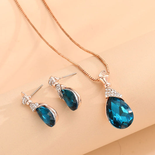 Rose gold tone bridal jewelry set with a necklace and stud earrings, each featuring a large blue teardrop gem and clear accents. - Image 9