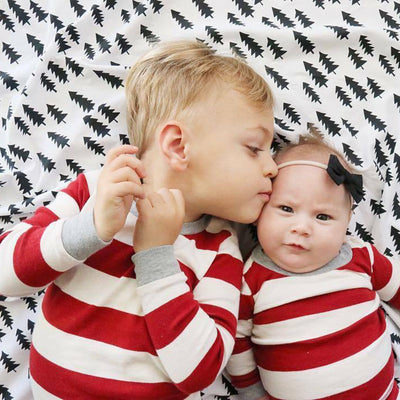 Family of four in matching red and white striped Christmas pajamas, sitting on a white rug with holiday decor. - Image 2