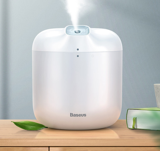 White Baseus car small elephant atomizer actively misting, shown on a wooden surface with a green leaf.