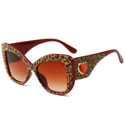 Leopard print cat-eye sunglasses with a red frame, gradient brown lenses, and a red heart embellishment.