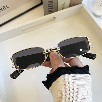 Black rectangular sunglasses with dark lenses and a thin metal frame, held by a hand against a light background. - Image 3