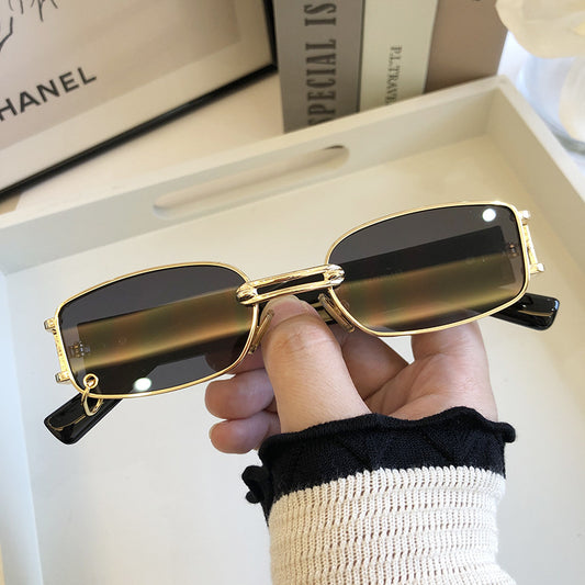 Black rectangular sunglasses with dark lenses and a thin metal frame, held by a hand against a light background.