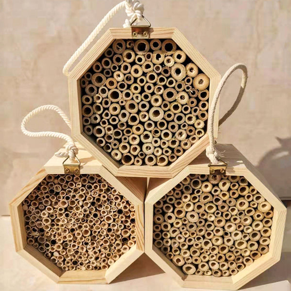 Three hexagonal wooden bee breeding boxes, filled with bamboo tubes, stacked together. The top box has a rope handle.
