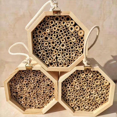 Three hexagonal wooden bee breeding boxes, filled with bamboo tubes, stacked together. The top box has a rope handle.