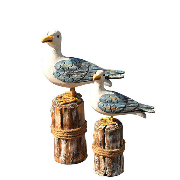 Set of two carved wooden seagull figurines on distressed posts with rope, featuring white, blue, and orange colors.