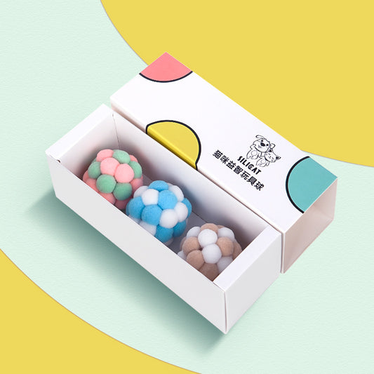 Three plush elastic bell balls for cats in a white gift box. Balls are pink/green, blue/white, and brown/white.