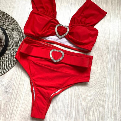 Red high-waisted two-piece bikini with a bandeau top and heart-shaped rhinestone buckles, displayed on a wooden surface. - Image 11
