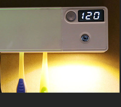 White toothbrush disinfector with UV light, USB cable, alcohol prep pad, and mounting strips on a light blue background.