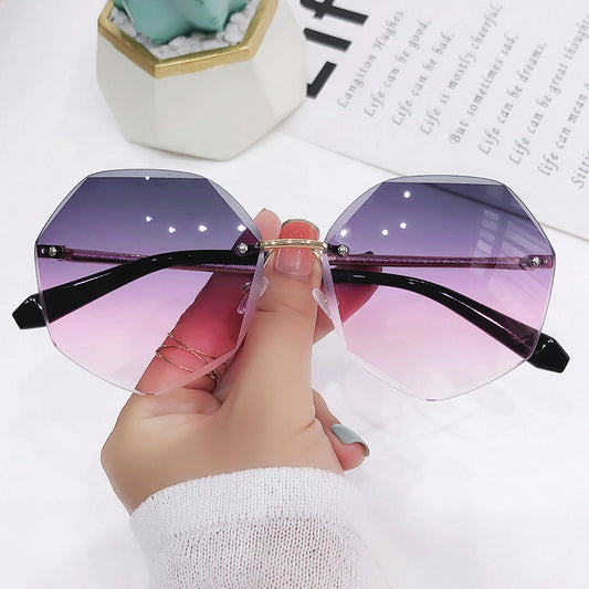 Ladies' cut-edge polygonal sunglasses with gradient purple-to-pink lenses and black temples, held by a hand.