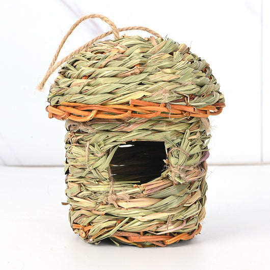 Hand-woven straw bird's nest with a round entrance, made from green and brown grass, hanging from a tree branch. - Image 8
