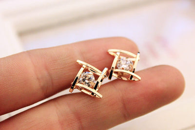 Gold-tone square stud earrings with clear zircon gemstones set in a hollow tic-tac-toe geometric frame. - Image 6