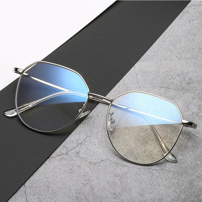 Black metal-framed glasses with irregular polygonal shape and anti-blue light lenses on a two-tone gray and black surface. - Image 7