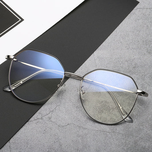 Black metal-framed glasses with irregular polygonal shape and anti-blue light lenses on a two-tone gray and black surface. - Image 8