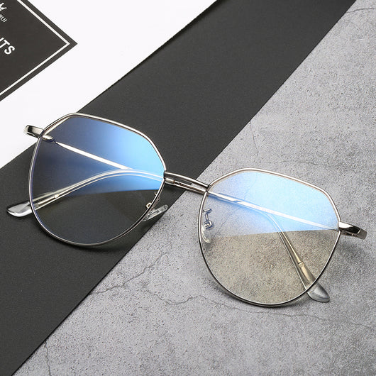 Black metal-framed glasses with irregular polygonal shape and anti-blue light lenses on a two-tone gray and black surface. - Image 9