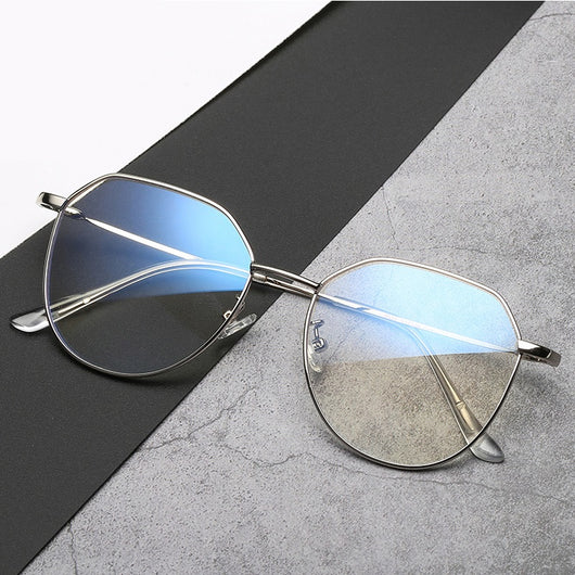 Black metal-framed glasses with irregular polygonal shape and anti-blue light lenses on a two-tone gray and black surface. - Image 5