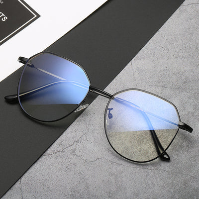 Black metal-framed glasses with irregular polygonal shape and anti-blue light lenses on a two-tone gray and black surface.