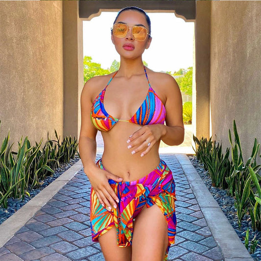 Woman wearing a vibrant multi-color abstract print three-piece bikini set with a matching sheer sarong on a balcony. - Image 2