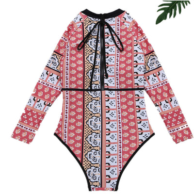 Woman in a red, orange, and cream floral long-sleeved one-piece swimsuit with black trim on a sandy beach. - Image 8