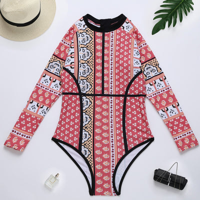 Woman in a red, orange, and cream floral long-sleeved one-piece swimsuit with black trim on a sandy beach. - Image 4