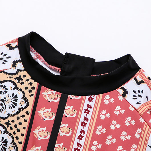 Woman in a red, orange, and cream floral long-sleeved one-piece swimsuit with black trim on a sandy beach. - Image 12
