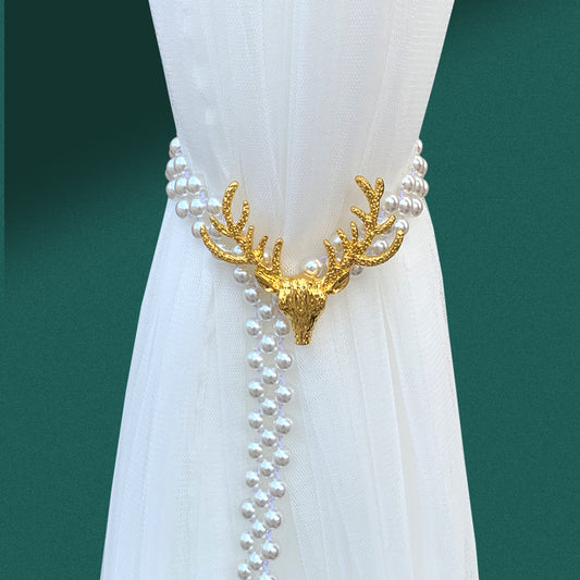 Silver elk head curtain tie-back with faux pearl strands holding back a sheer white curtain.