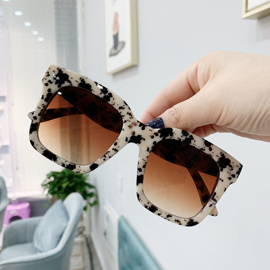 Retro oversized square sunglasses with a dark red frame and pink gradient lenses, held by a hand.
