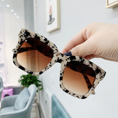 Retro oversized square sunglasses with a dark red frame and pink gradient lenses, held by a hand.